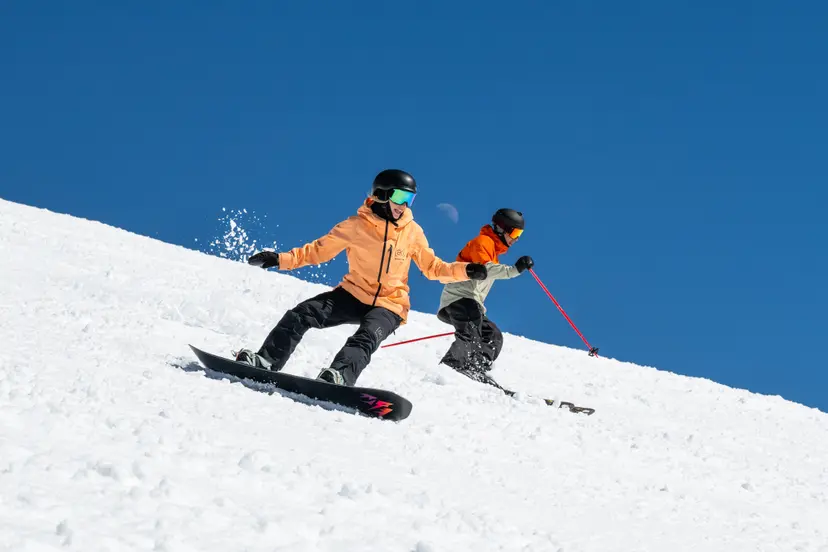 skier and snowboarder skiing with half moon in background